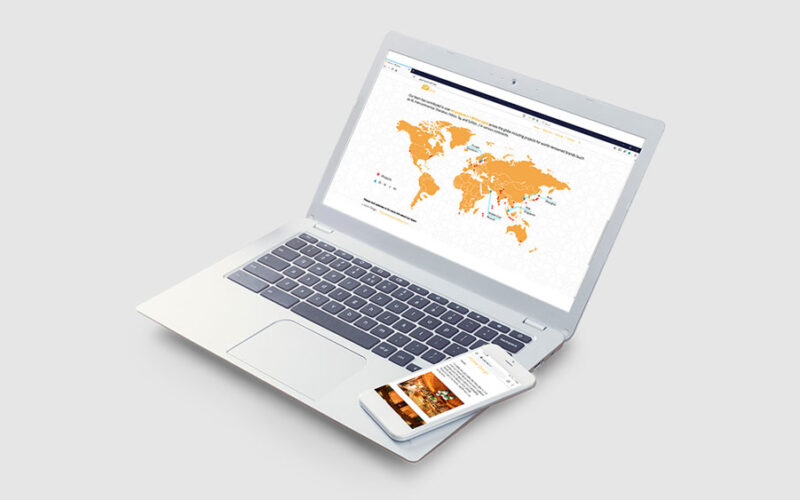 Open laptop and a smartphone on a grey surface, the laptop displaying a website with an orange world map
