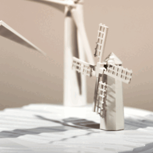 Animated white paper model of a windmill with turning sails, photographed close up against a soft grey background