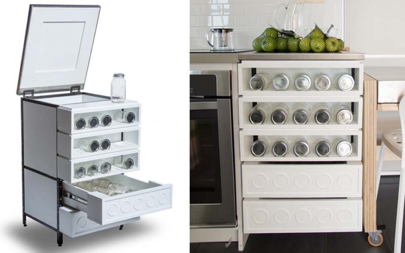 White freestanding kitchen cabinet with a lifted lid and pull-out drawers holding rows of glass preserving jars, shown as a render and installed in a kitchen beside an oven