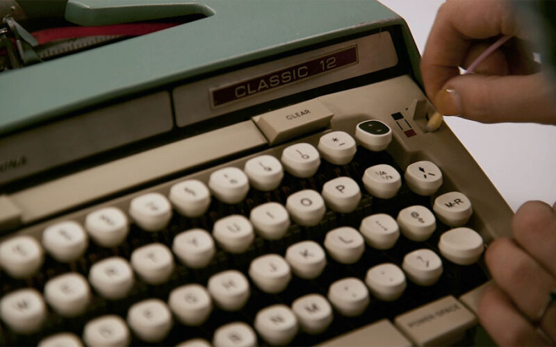 Close-up of a cream-coloured Classic 12 typewriter with a hand pressing one of its round keys