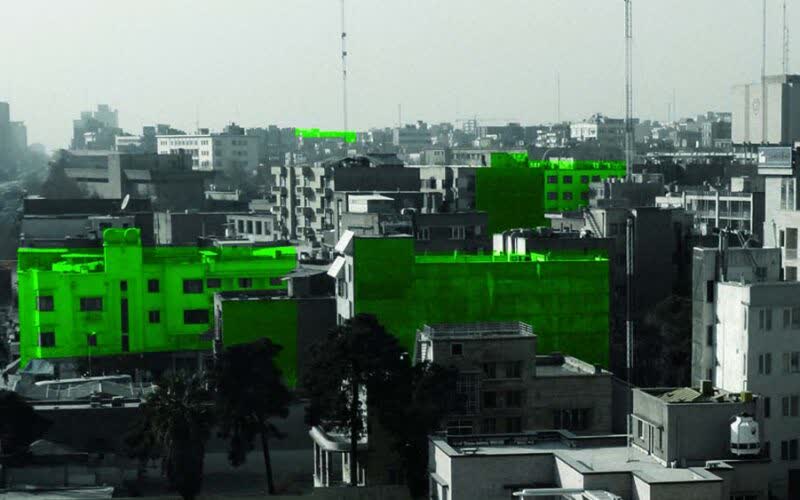Black-and-white view over dense Tehran rooftops with the blank side walls of buildings highlighted in bright green